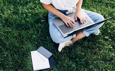 student girl with laptop outdoors sitting on the grass, surfing the internet or preparing for exams. Technology, education and remote work concept. Soft selective focus.